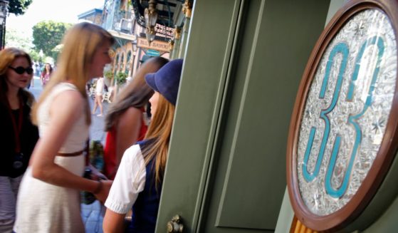 A guest relations guide holds open the door to Club 33 for visitors on a special paid VIP tour, 