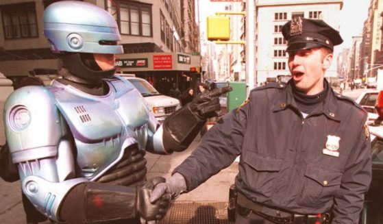 New York City Police Officer Paul Dean, right, gets a handshake from a person dressed as "RoboCop," left, outside the Toy Fair in New York City.