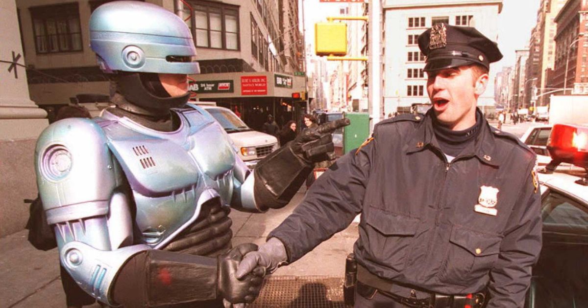 New York City Police Officer Paul Dean, right, gets a handshake from a person dressed as "RoboCop," left, outside the Toy Fair in New York City.