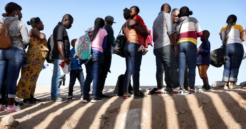 Immigrants from Haiti, who crossed through a gap in the U.S.-Mexico border barrier, wait in line to be processed by the U.S. Border Patrol on May 20, 2022 in Yuma, Arizona.