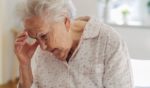 This stock image shows an elderly lady experiencing confusion and holding her head.