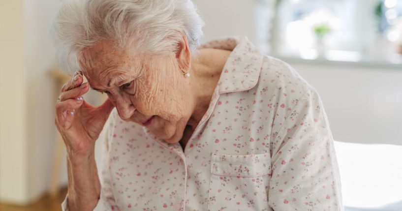 This stock image shows an elderly lady experiencing confusion and holding her head.