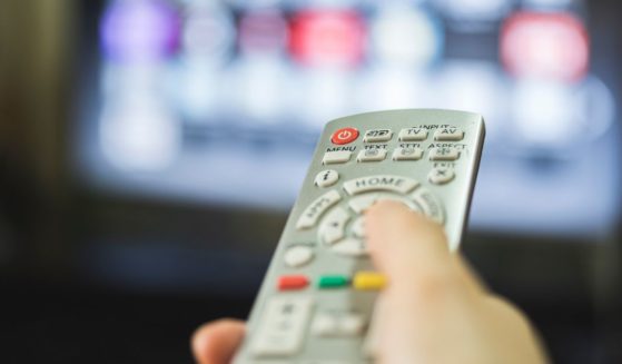 This stock image shows a person using a TV remote to change the channel.