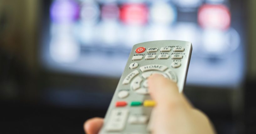 This stock image shows a person using a TV remote to change the channel.