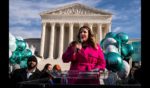 Lorie Smith, a Christian graphic artist and website designer in Colorado, center in pink, speaks to supporters outside the Supreme Court on Monday, Dec. 5, 2022 in Washington, DC.