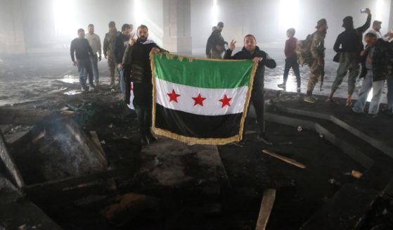 Rebel fighters stand with the flag of the revolution on the burnt gravesite of Syria's late president Hafez al-Assad at his mausoleum in the family's ancestral village of Qardaha, Syria, on Wednesday.