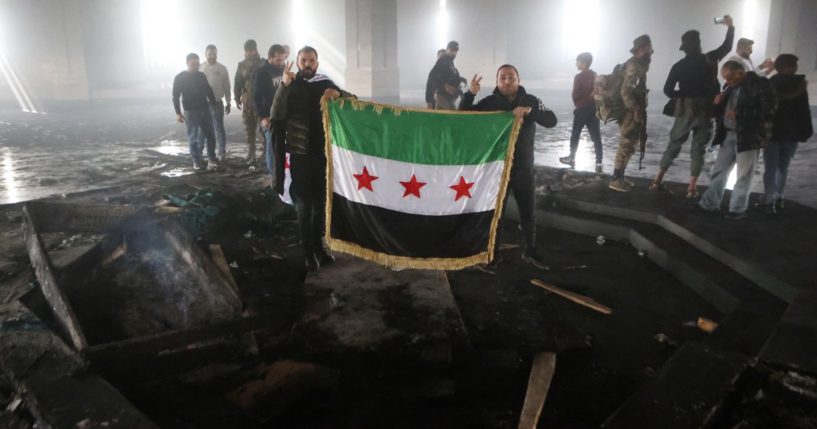 Rebel fighters stand with the flag of the revolution on the burnt gravesite of Syria's late president Hafez al-Assad at his mausoleum in the family's ancestral village of Qardaha, Syria, on Wednesday.