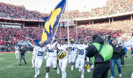 Quinton Johnson #28, Raheem Anderson #62, Tavierre Dunlap #22, and Keshaun Harris #36 of the Michigan Wolverines run to plant the Michigan flag at center field after a college football game against the Ohio State Buckeyes in Columbus, Ohio, on Nov. 30.