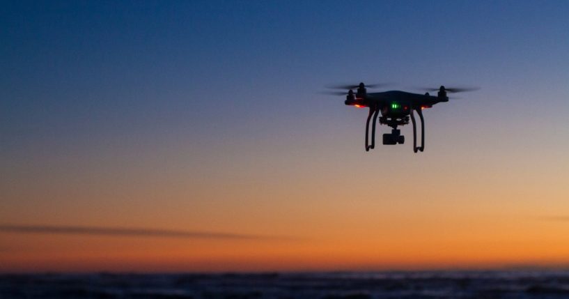 This stock image shows a drone flying over the ocean at sunrise.