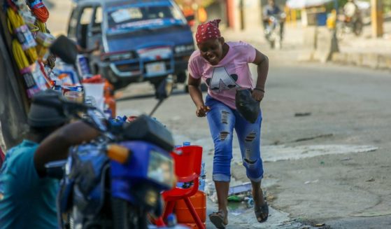 A woman runs for cover amid gunfire during clashes between police and gangs in Port-au-Prince, Haiti, Monday. Gang members killed at least 184 people, mostly elderly, over the weekend.