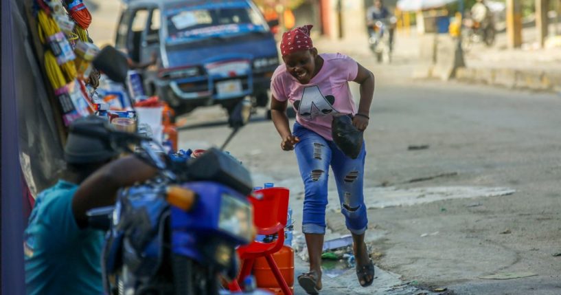 A woman runs for cover amid gunfire during clashes between police and gangs in Port-au-Prince, Haiti, Monday. Gang members killed at least 184 people, mostly elderly, over the weekend.