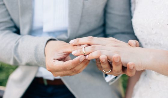 This stock image shows a groom placing a wedding ring onto his bride's finger.