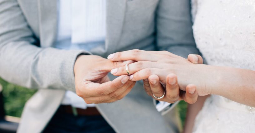 This stock image shows a groom placing a wedding ring onto his bride's finger.