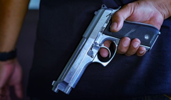 Stock photograph of a hand holding a semiautomatic pistol behind the back.