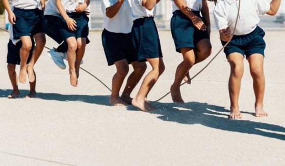 A class of young children practice jump roping, barefoot, with their teacher.