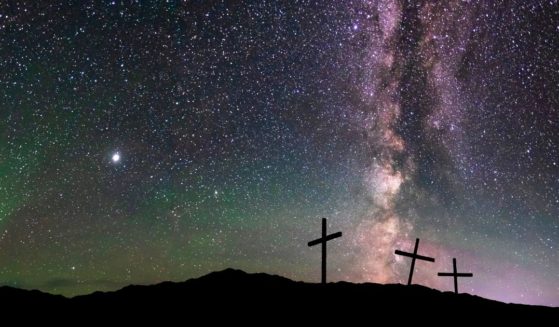 Three crosses on a hill at night under the starry sky.