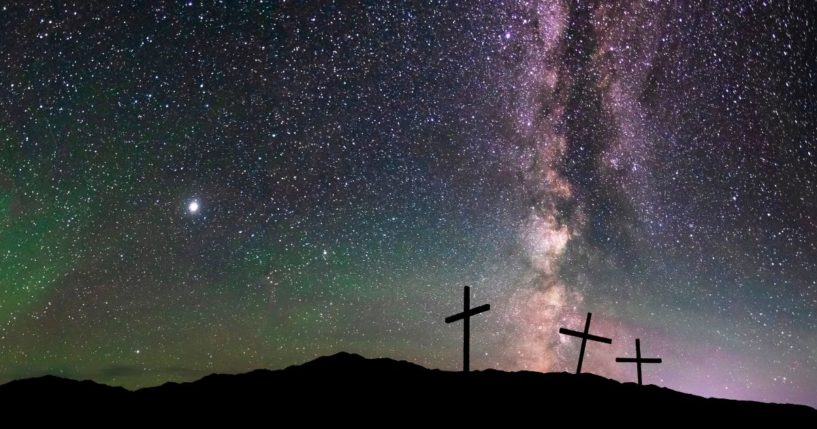 Three crosses on a hill at night under the starry sky.