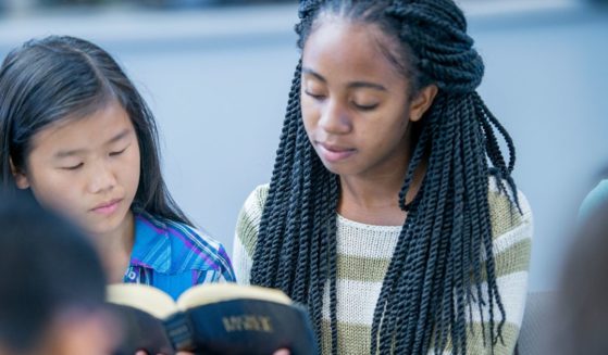 A high school age girl is holding the Bible and reading it with her fellow classmates during a Bible study.