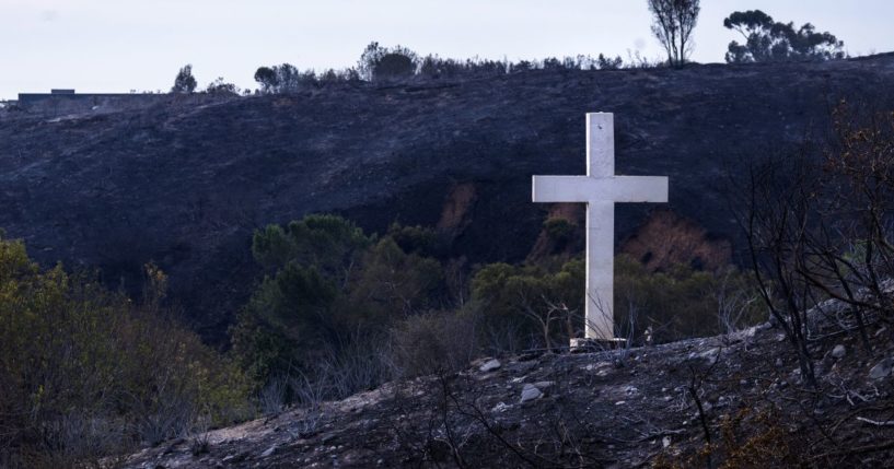 A cross stands amidst brush charred by fire across from Pepperdine University.