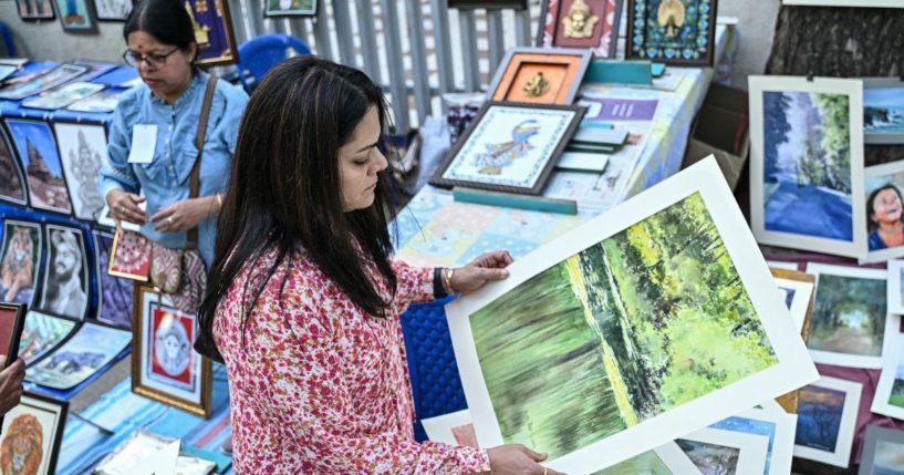 A visitor looks at paintings on display for sale at a roadside stall during 