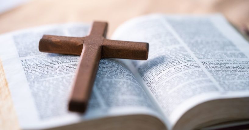 This stock image shows a cross resting on top of an open Bible.