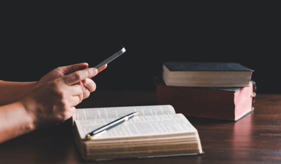 This stock image shows a Christian with an open Bible and their phone, studying the Scripture.