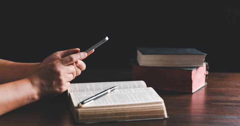 This stock image shows a Christian with an open Bible and their phone, studying the Scripture.