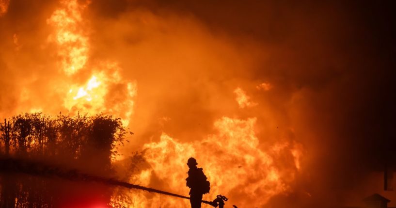 A firefighter stands on top of a fire truck to battle the Palisades Fire while it burns homes on the Pacific Coast Highway amid a powerful windstorm Los Angeles, California, on Jan. 8.