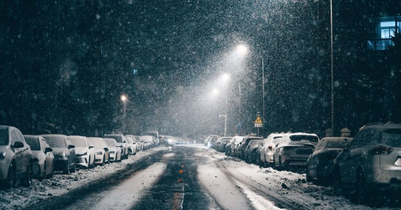 This stock image shows snow falling on a street at night.