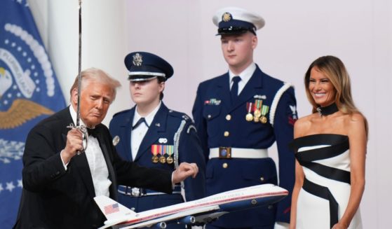 President Donald Trump, left, uses a saber to cut a cake at the Commander in Chief Inauguration Ball on Monday while first lady Melania Trump, right, looks on in delight.