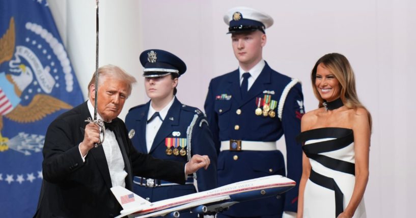 President Donald Trump, left, uses a saber to cut a cake at the Commander in Chief Inauguration Ball on Monday while first lady Melania Trump, right, looks on in delight.