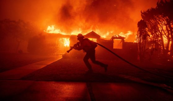 A firefighter battles the Palisades Fire as it burns a structure in the Pacific Palisades neighborhood of Los Angeles Tuesday.