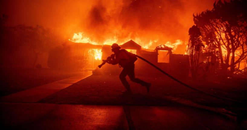 A firefighter battles the Palisades Fire as it burns a structure in the Pacific Palisades neighborhood of Los Angeles Tuesday.