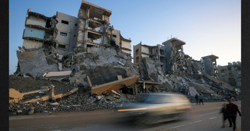 Pedestrians and cars pass by apartments destroyed by Israeli army strikes in the central Gaza Strip town of Khan Younis Wednesday. One such strike killed a Hamas leader who commanded a battalion that slaughtered dozens of civilians in the Israeli Kibbutz Nir Oz on Oct. 7, 2023