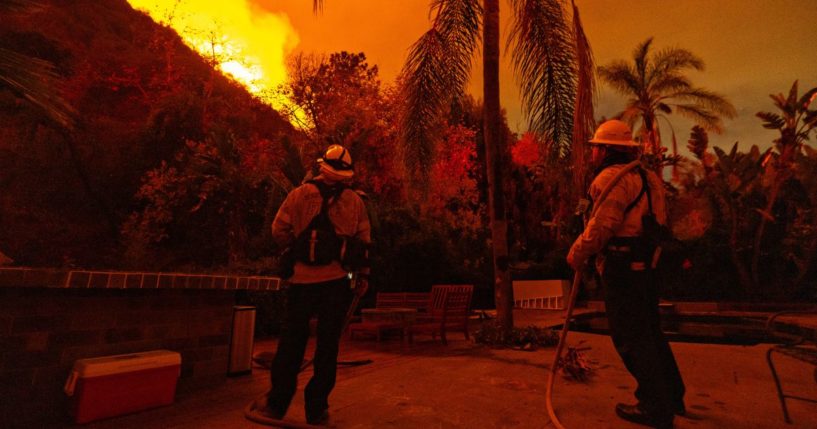 Firefighters stand guard at a home on Mandeville Canyon road as the Palisades fire spreads towards Encino on Saturday.