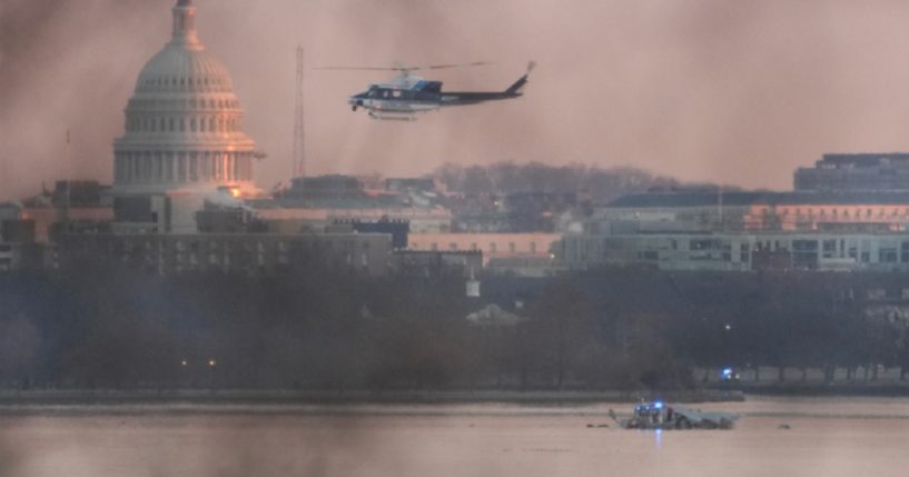 A helicopter flies Thursday morning near the crash site of the American Airlines plane on the Potomac River after the plane collided with an Army helicopter on approach to Reagan National Airport on Wednesday night in Arlington, Virginia.