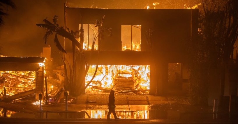 A firefighter watches the flames from the Palisades Fire burning homes on the Pacific Coast Highway amid a powerful windstorm on January 8, 2025 in Los Angeles, California.