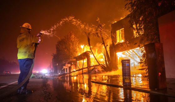 A firefighter battles the Palisades Fire while it burns homes at Pacific Coast Highway amid a powerful windstorm on January 8, 2025 in Los Angeles, California.