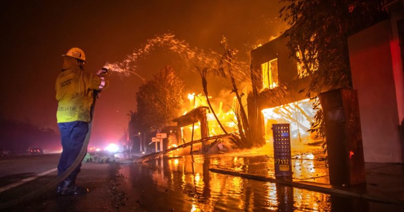 A firefighter battles the Palisades Fire while it burns homes at Pacific Coast Highway amid a powerful windstorm on January 8, 2025 in Los Angeles, California.