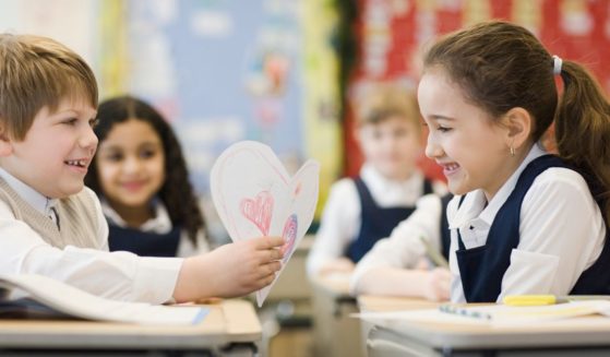 Two children celebrate Valentine's Day with the typical schoolroom traditions in a stock photograph.