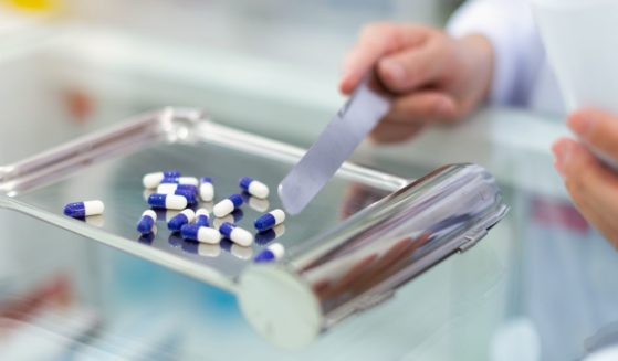 This stock image shows a pharmacist using a tray to count and dispense pills in a pharmacy.