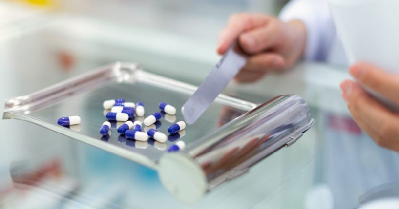 This stock image shows a pharmacist using a tray to count and dispense pills in a pharmacy.