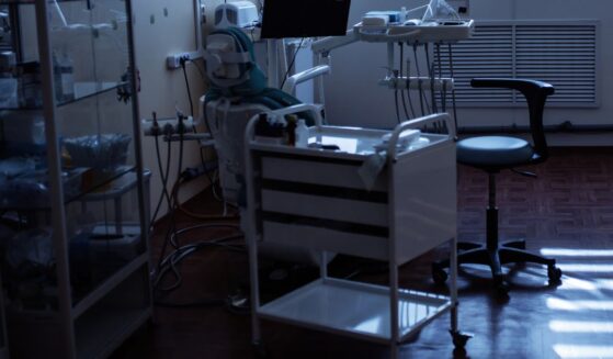A dental chair surrounded by dental equipment is pictured in a dark room.